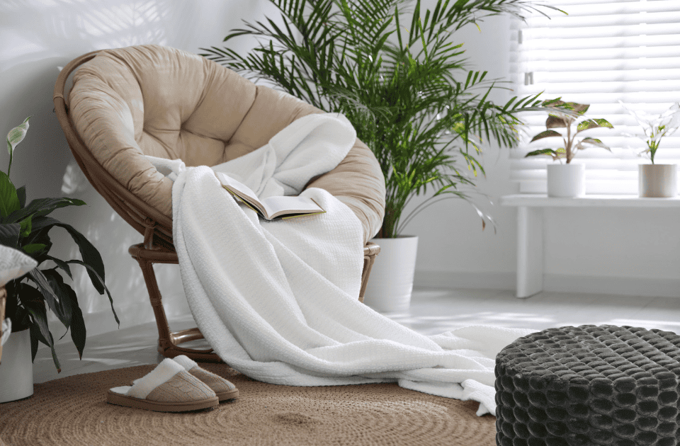 Cozy indoor reading corner with chair, blanket, and plants.