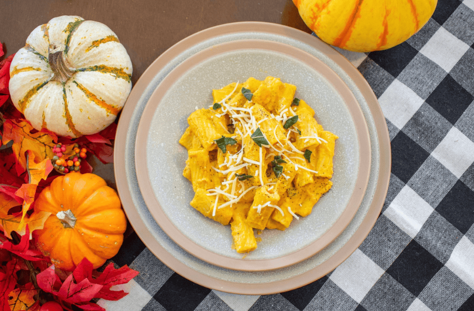 Pumpkin pasta with sage served on a plate with autumn decorations around.